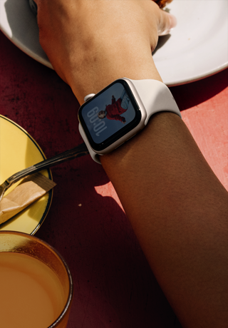 A person's arm grabbing a breakfast food, Apple Watch SE 3 on wrist, Starlight aluminium case, always-on display, portrait of a person on watch face, starlight Sport Band